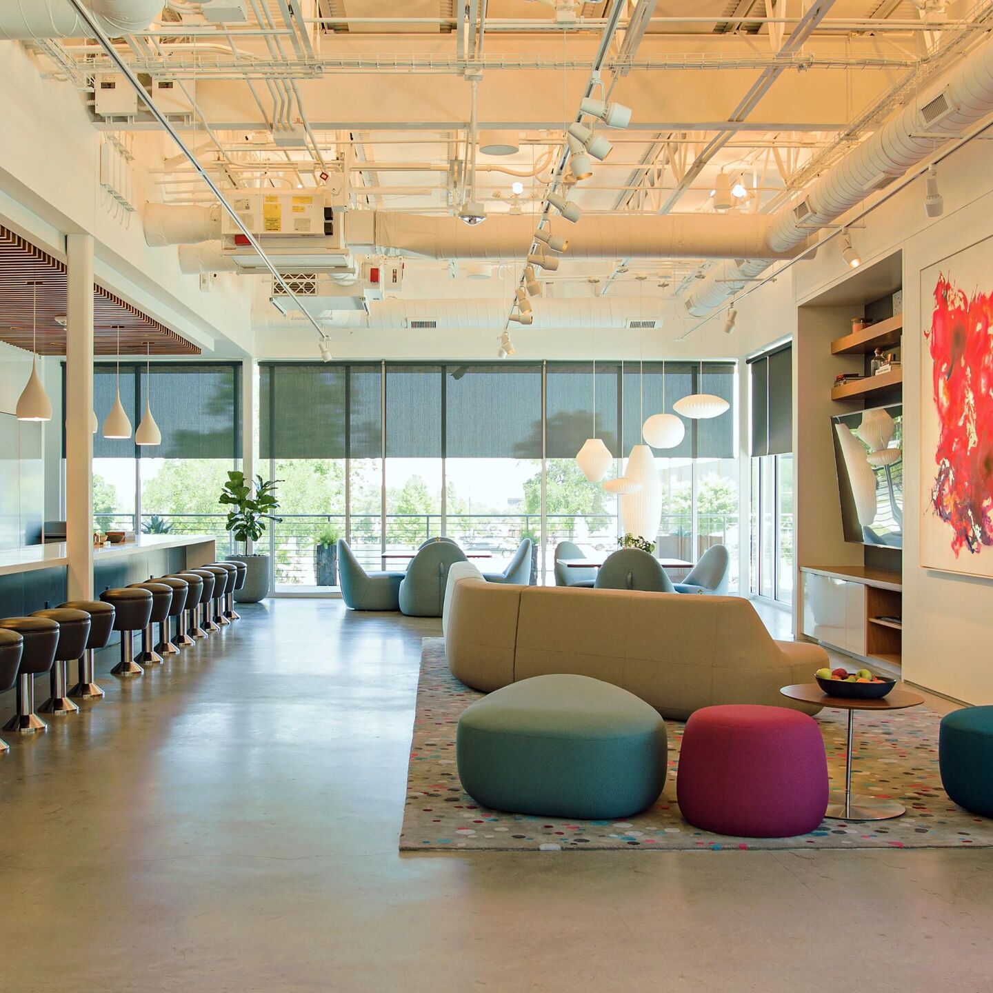 Modern office space featuring integrated track and lamp lighting with warm ambient illumination and natural light from large windows